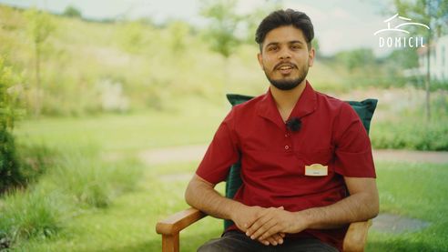 Auszubildender Sanam Kumar sitzt im Freien auf einem Stuhl in einem Interview 